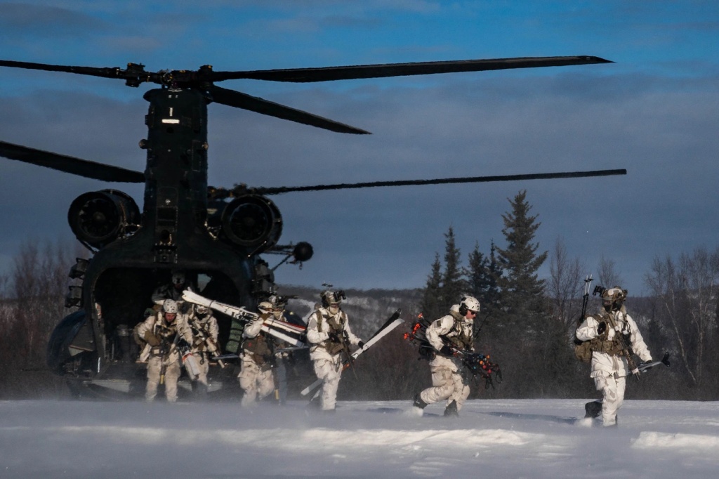 Modern-day soldiers exiting a large military helicopter carrying skis and combat equipment in preparation for combat exercises.